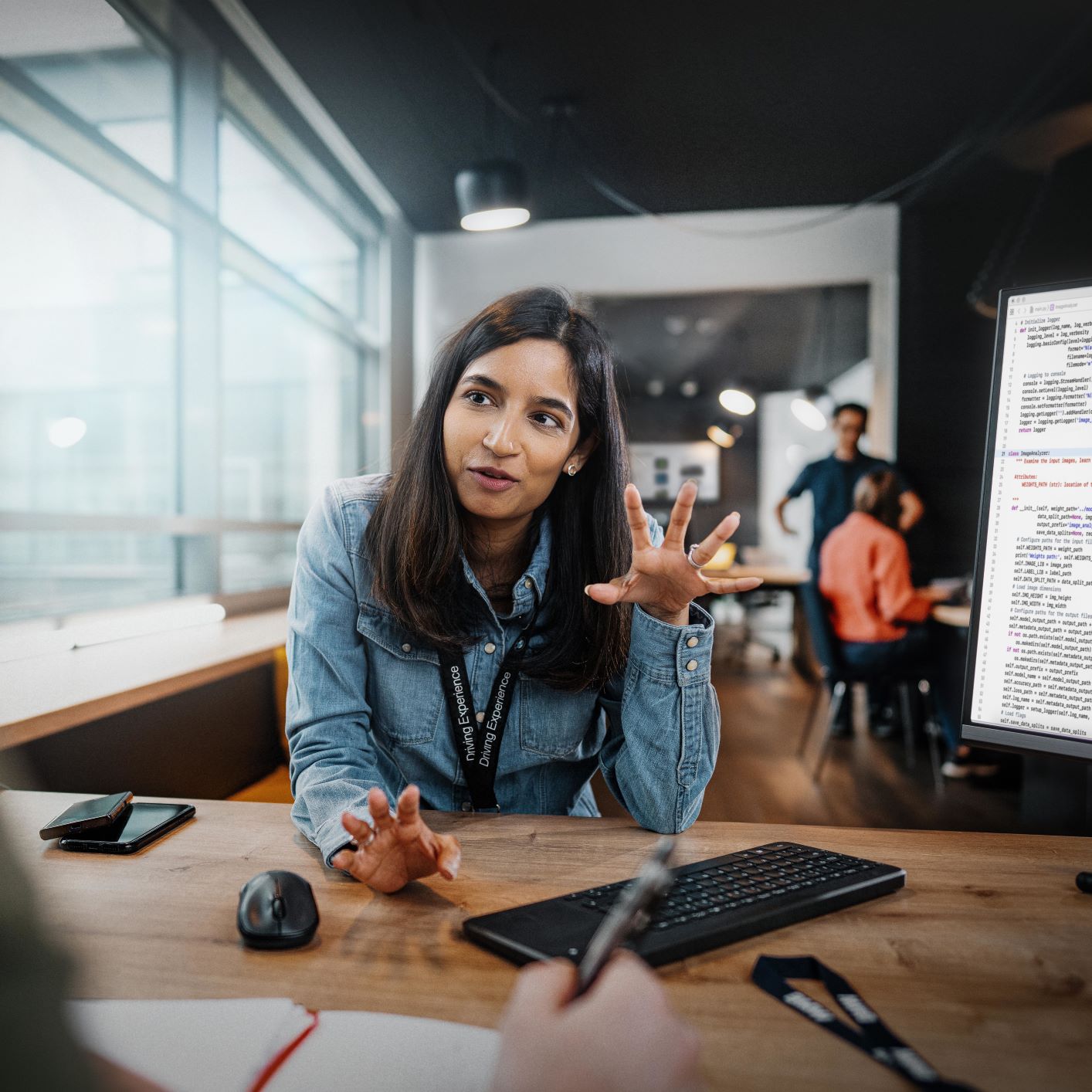 The picture shows a woman working in IT at BMW explaining something to two colleagues.