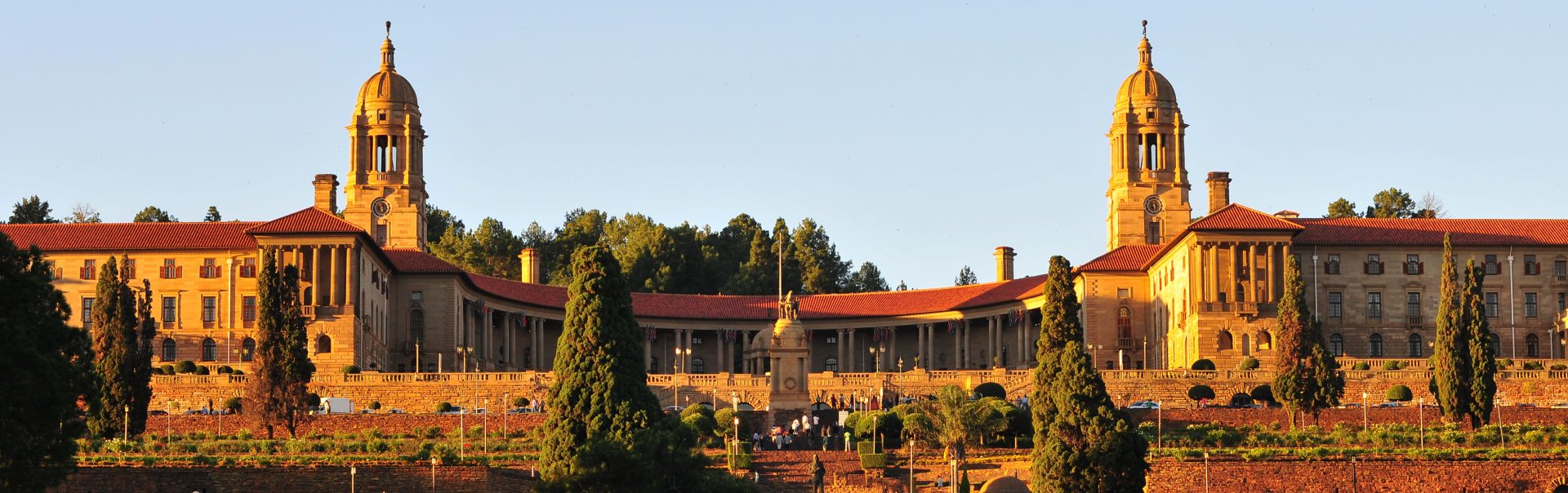 "South African Union Buildings seen here at sundown. The Union Buildings were built from light sandstone and designed by the Sir Herbert Baker in the English monumental style. The Buildings are over 275 m long and a semi-circular shape, with the two wings at the sides that represent the union of a formerly divided people. (English and Afrikaans). The Union Buildings are considered by many to be the architect's greatest achievement and a South African architectural masterpiece. The cornerstone was laid in November 1910. Requiring over 1,265 workers over 3 years to build, the structure was completed in 1913. Today, the official seat of the South African government and also the offices of the President of South Africa."