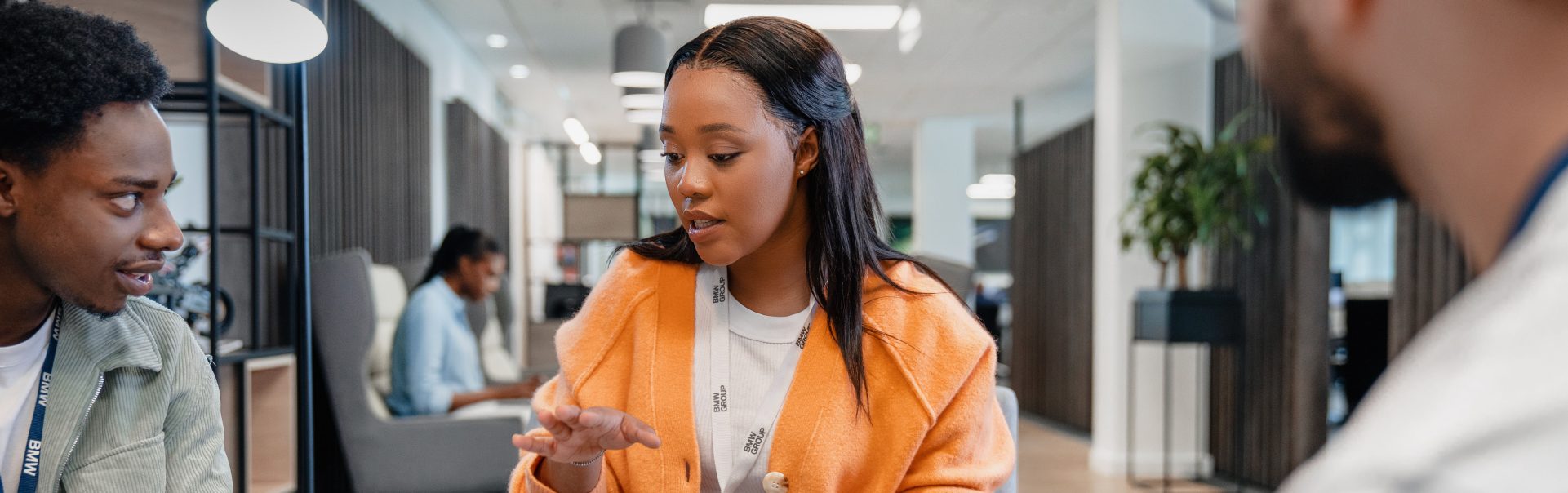 Three colleagues at the BMW Group are having a conversation in a modern office setting.